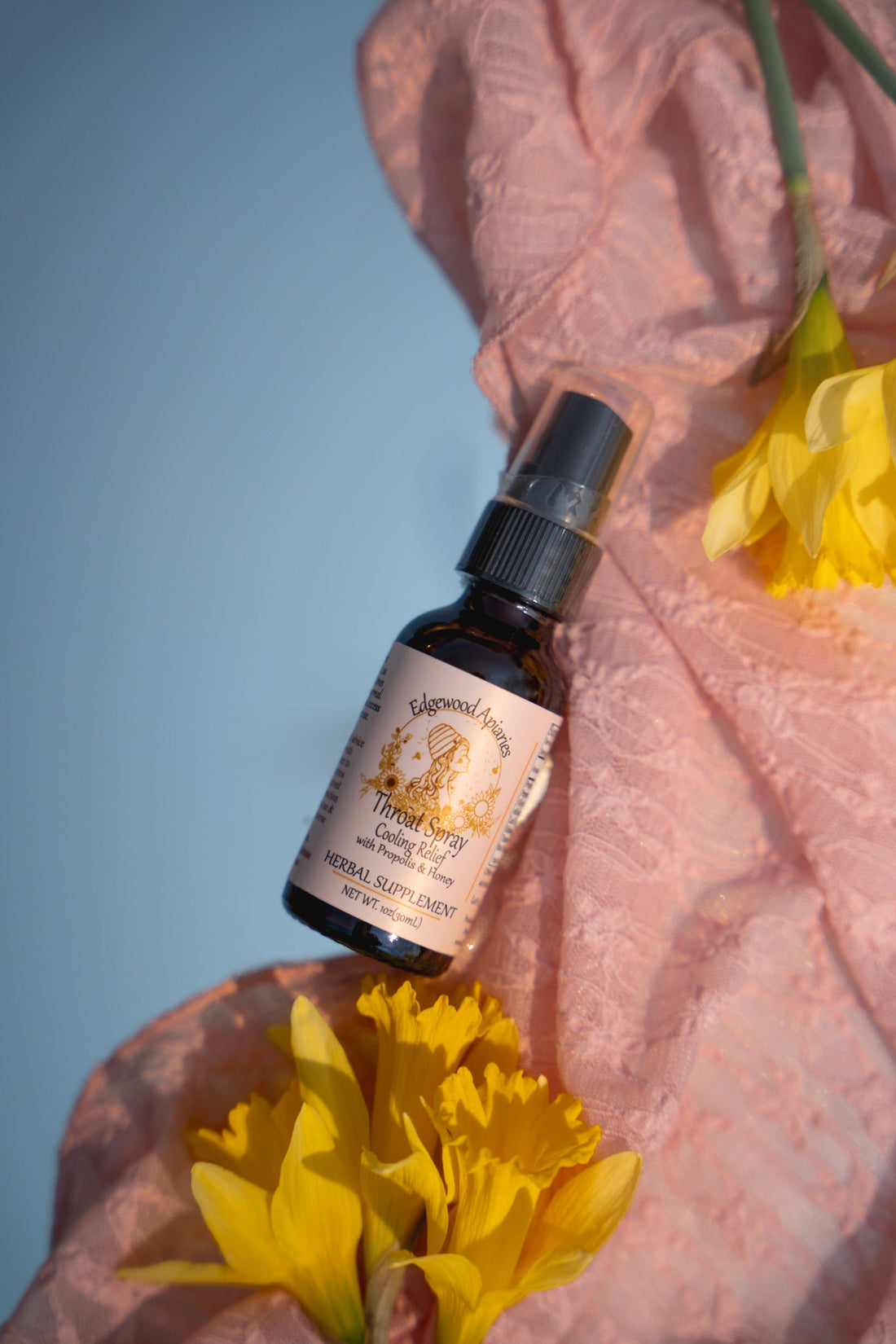 Edgewood Apiaries Cooling Relief throat spray with propolis and honey. 1 oz amber bottle on pink lace with daffodils.