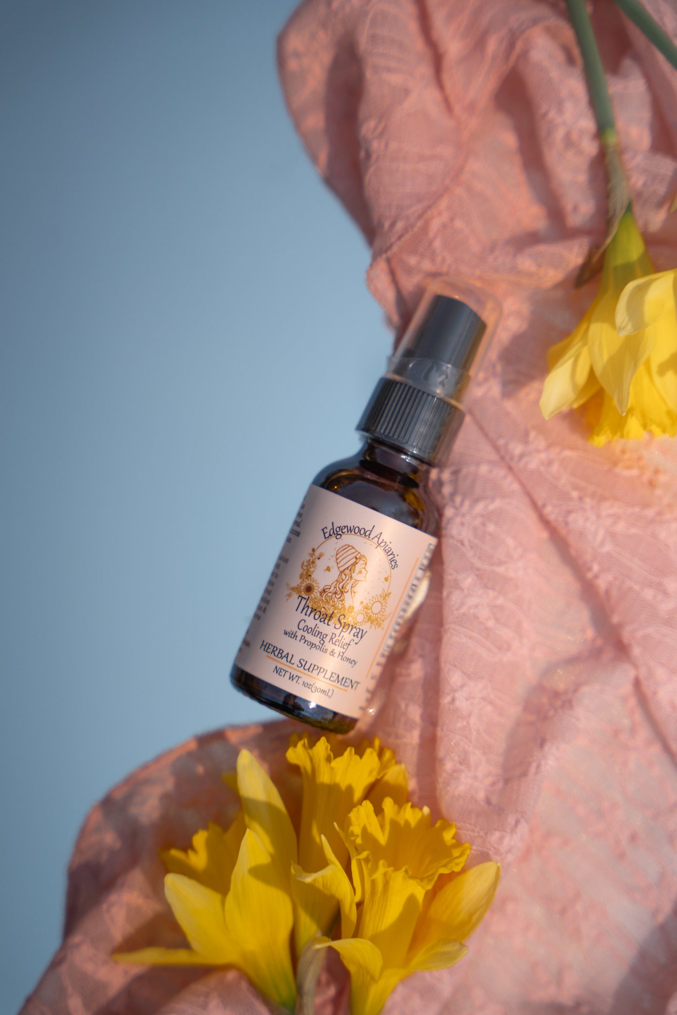 Edgewood Apiaries Cooling Mist throat spray with propolis and honey (label: Cooling Relief). 1 oz amber bottle on pink lace with daffodils.