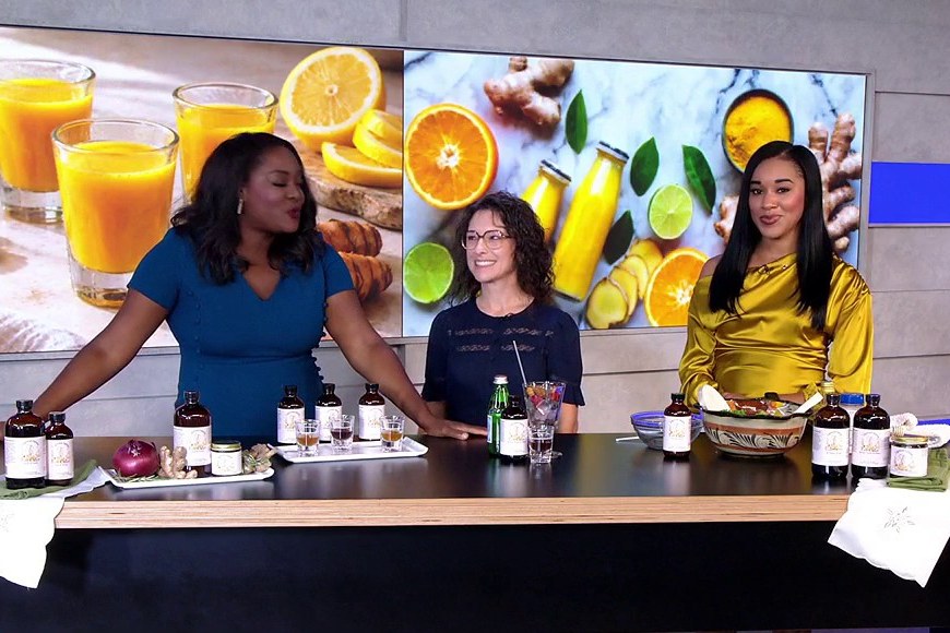 Three women at a Good Day DC studio table set with amber bottles, small jars and tasting glasses. Still from FOX 5 DC.